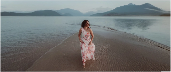 frau im blumigen kleid am strand mit bergblick