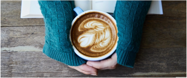 haende halten eine tasse kaffee mit kunstwerk