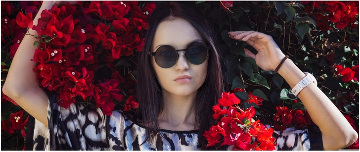junge frau mit sonnenbrille vor bluehenden blumen