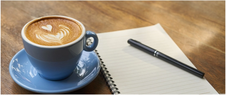 kaffee mit latte art und notizbuch auf holz