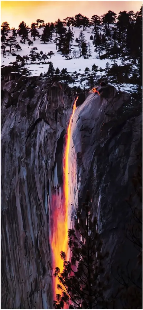 leuchtender wasserfall im abendlicht ueber schneebedeckten bergen