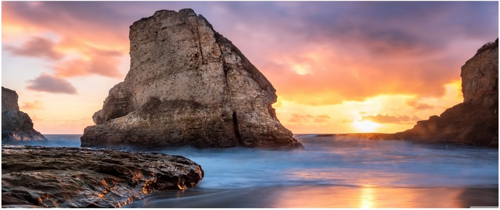 sonnenuntergang ueber kuestenlandschaft mit felsen und wellen