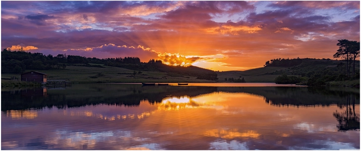 sonnenuntergang ueber ruhigem see mit waeldern