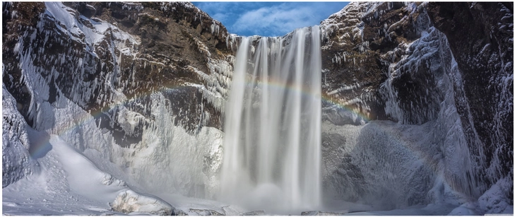 wasserfall mit regenbogen in winterlicher landschaft