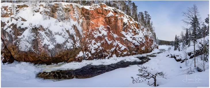 winterlandschaft mit gefrorenem fluss und roter felswand